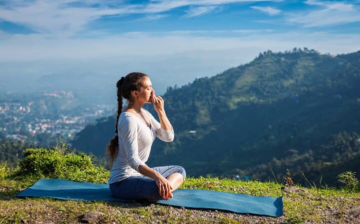 A woman practicing a seated breathing exercise outdoors on a yoga mat