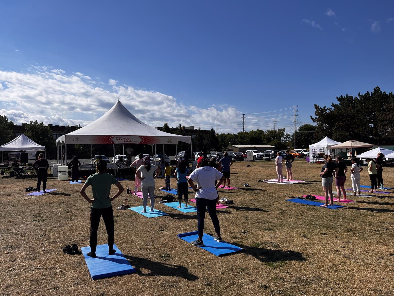 A group of festival visitors standing on yoga mats outdoors near the festival's tents during a group session