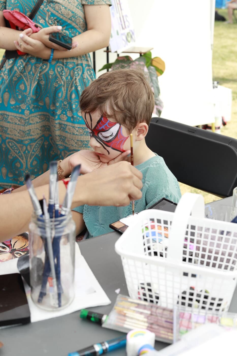 A young boy having a Spider-Man mask design face-painted by an artist at the festival's Kids Zone