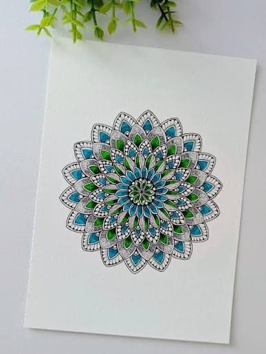 A hand-drawn and colored mandala design on paper, in blue and green